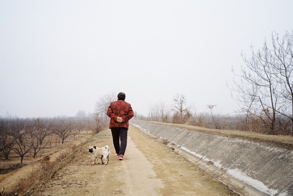 man in black jacket and black pants walking with white dog on road during daytime