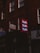 A dimly lit street scene features a series of signs attached to brick buildings. A prominent red sign with the word 'Nails' repeated three times in light letters stands out among other signs for a tailor and dry cleaner. The buildings give a sense of an urban environment.