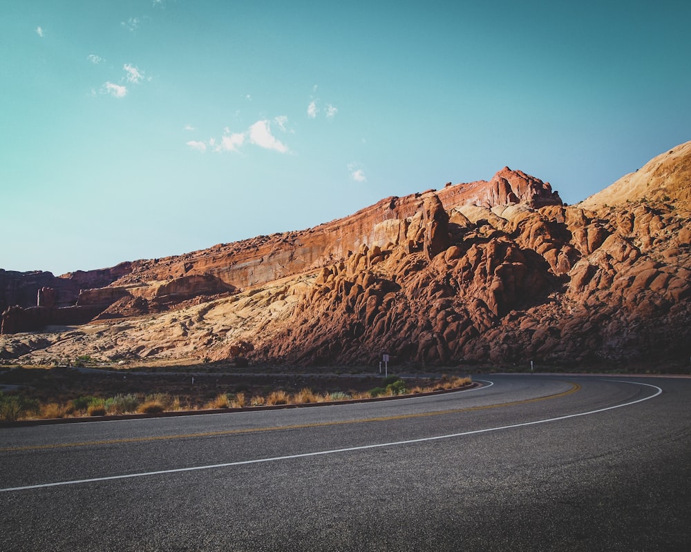 brown rock formation beside gray asphalt road during daytime