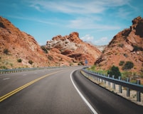 gray concrete road between brown rock formation under blue sky during daytime