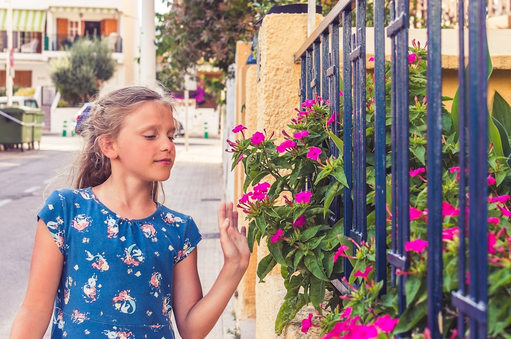 girl in blue and white floral crew neck t-shirt standing beside blue metal fence during