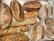 A selection of various artisanal breads placed on a surface. The loaves include different shapes and textures, such as baguettes and round boules, featuring rustic crusts and visible ingredients like olives.
