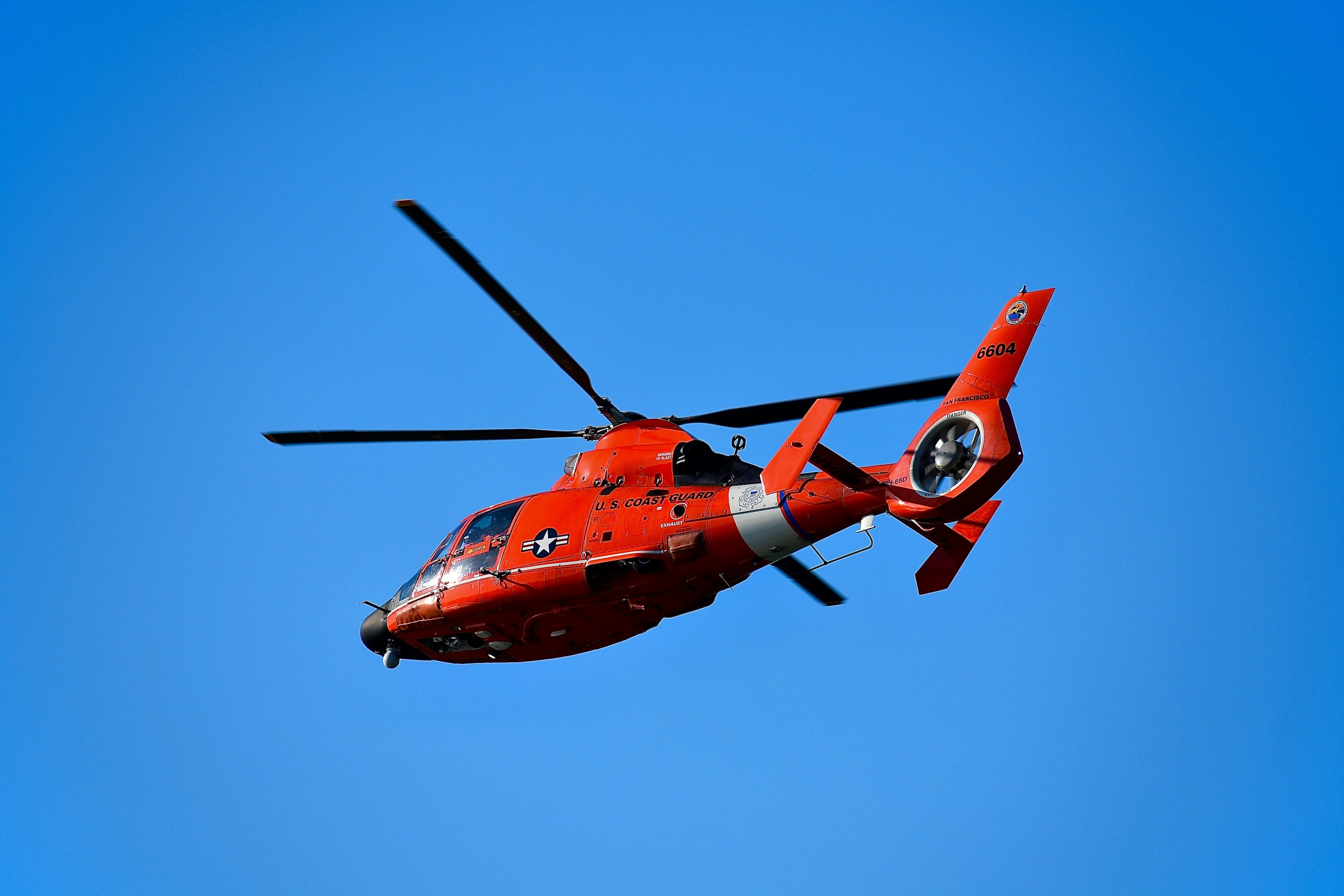 red and black helicopter flying in the sky, U.S. Coast Guard helicopter flying amongst blue sky during daytime