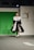A model walks down a runway wearing a striking black and white gown with voluminous sleeves and a high slit. The backdrop features a green screen with a logo for 'Prêt à México' and a reference to Maserati. The atmosphere suggests a fashion show setting with professional lighting.