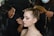 A makeup artist applies eyeliner to a young woman with her hair pulled back. Another person holds the woman's ponytail. The focus is on the detailed eye makeup, showing skillful artistry.