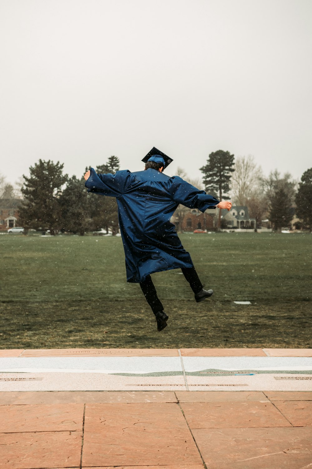 man in blue academic dress and black boots running on green grass field during daytime