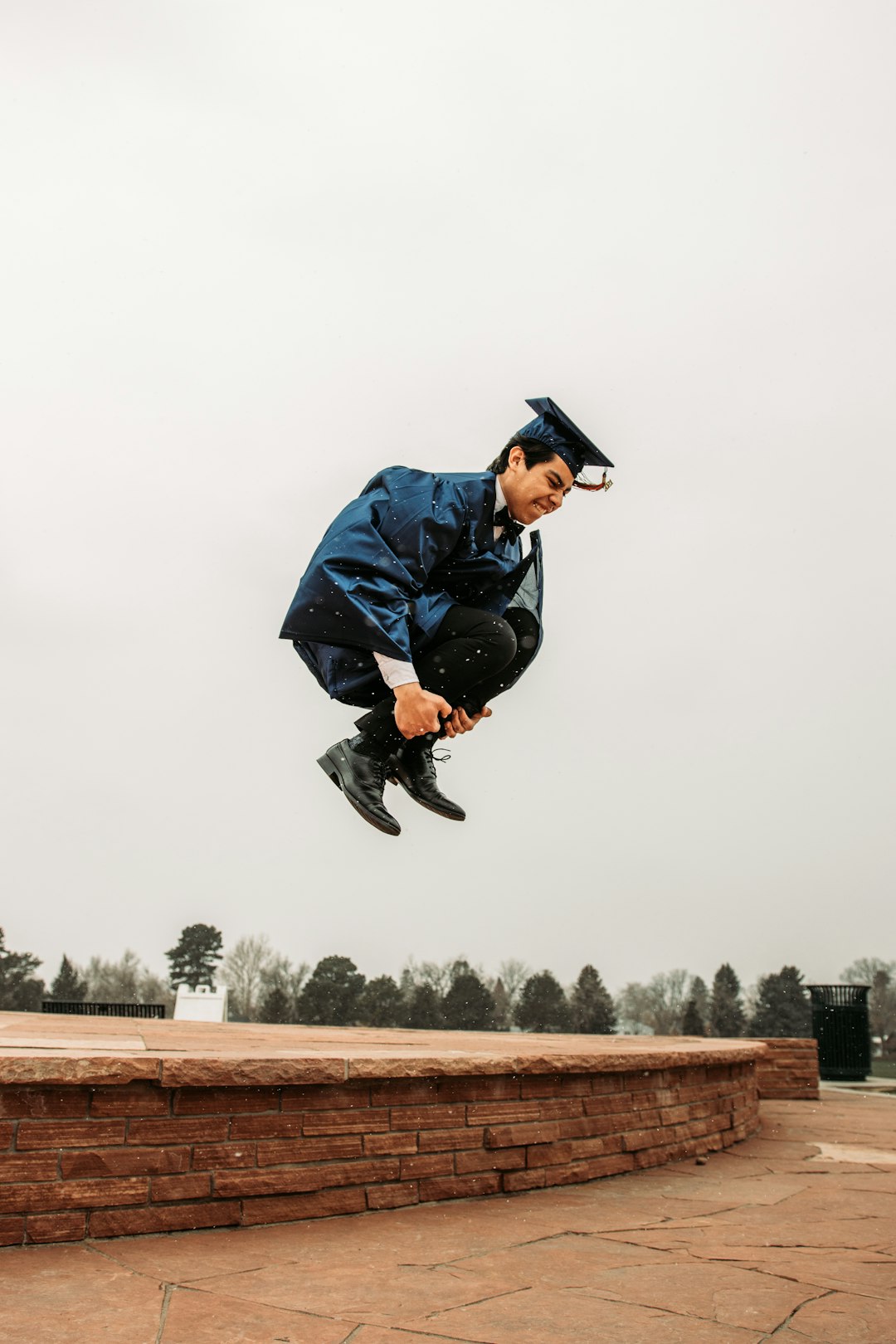 man in blue jacket and black cap jumping on brown concrete fence during daytime