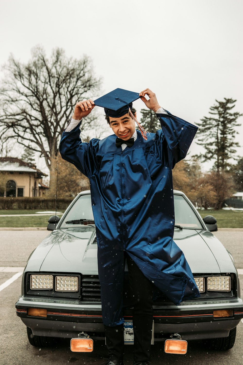 man in blue academic robe standing near white car