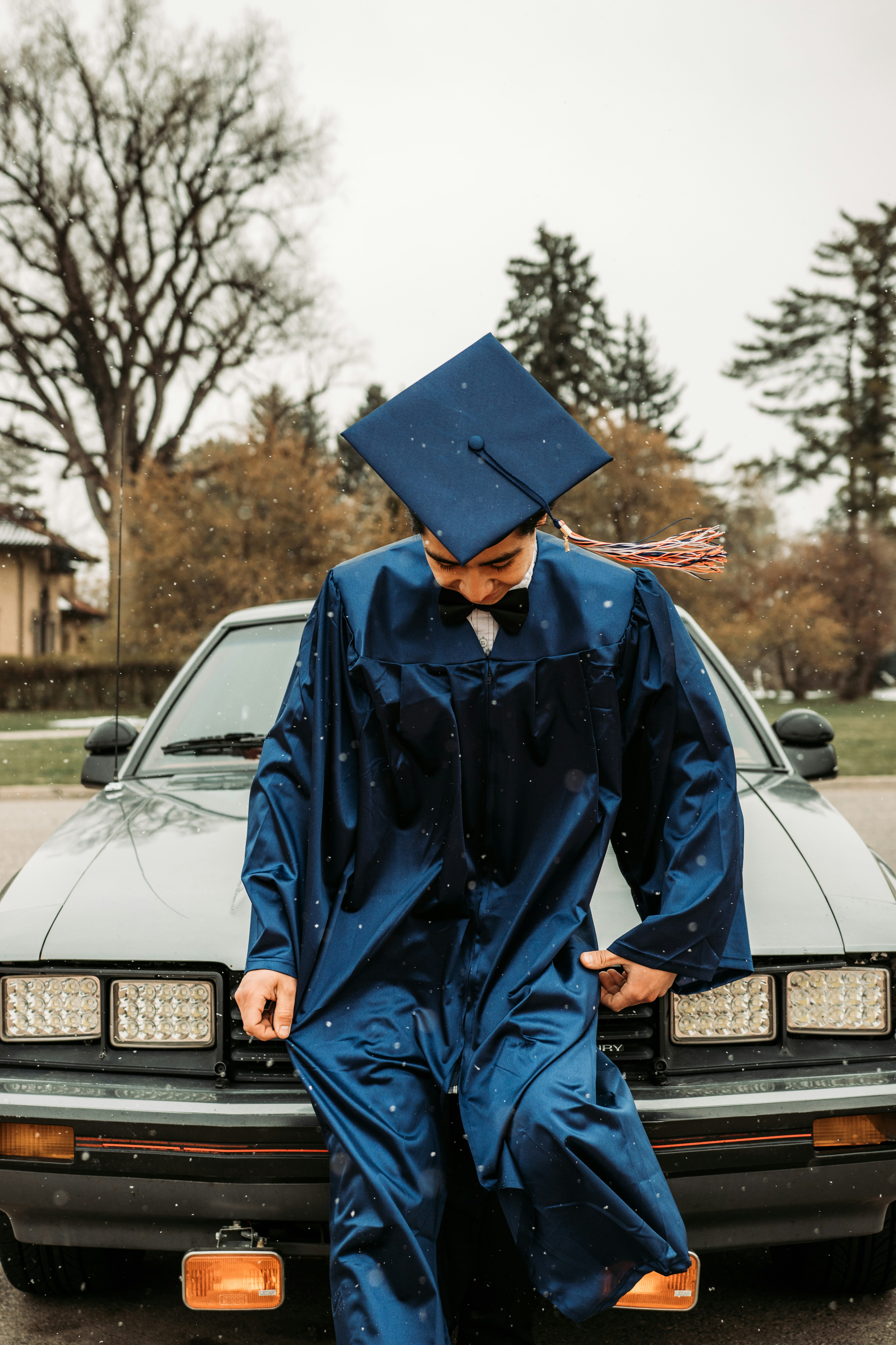man in blue academic robe sitting on black car hood during daytime