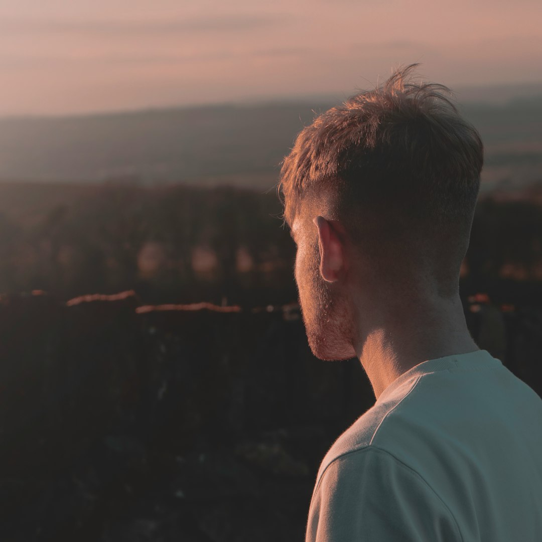 man in white crew neck shirt looking at the city during sunset