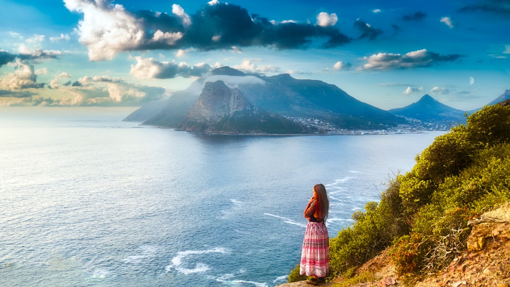 woman in pink and white plaid dress standing on green grass field near body of water