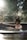 A person with their hair tied up is relaxing in a circular outdoor hot tub. Sunlight filters through surrounding trees, creating a tranquil and serene atmosphere. The background is blurred, emphasizing the calmness and natural setting.