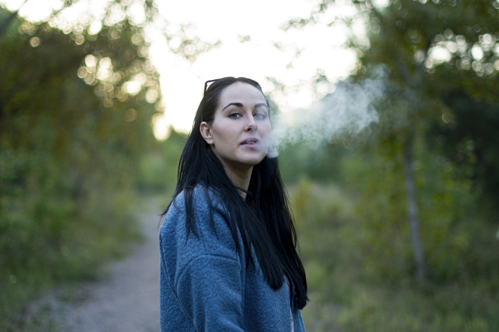 woman in blue turtleneck sweater standing near green trees during daytime