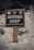A wooden sign with bold white letters reads 'Souvenir Shop' and 'Mementos as the memories of your visit' underneath. It is set against a backdrop of snow with several rocks partially visible at the bottom left corner.