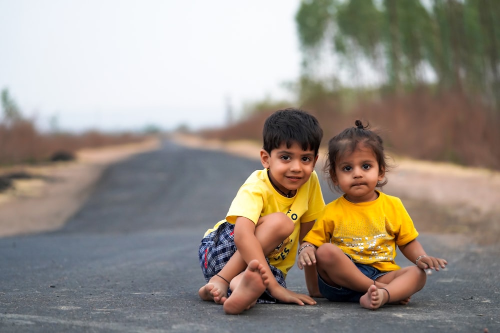 boy in yellow crew neck t-shirt sitting on gray concrete floor during daytime