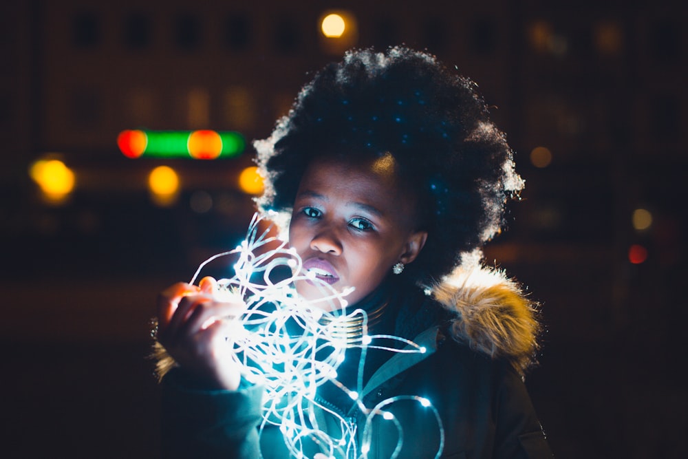 girl in black fur jacket holding string lights