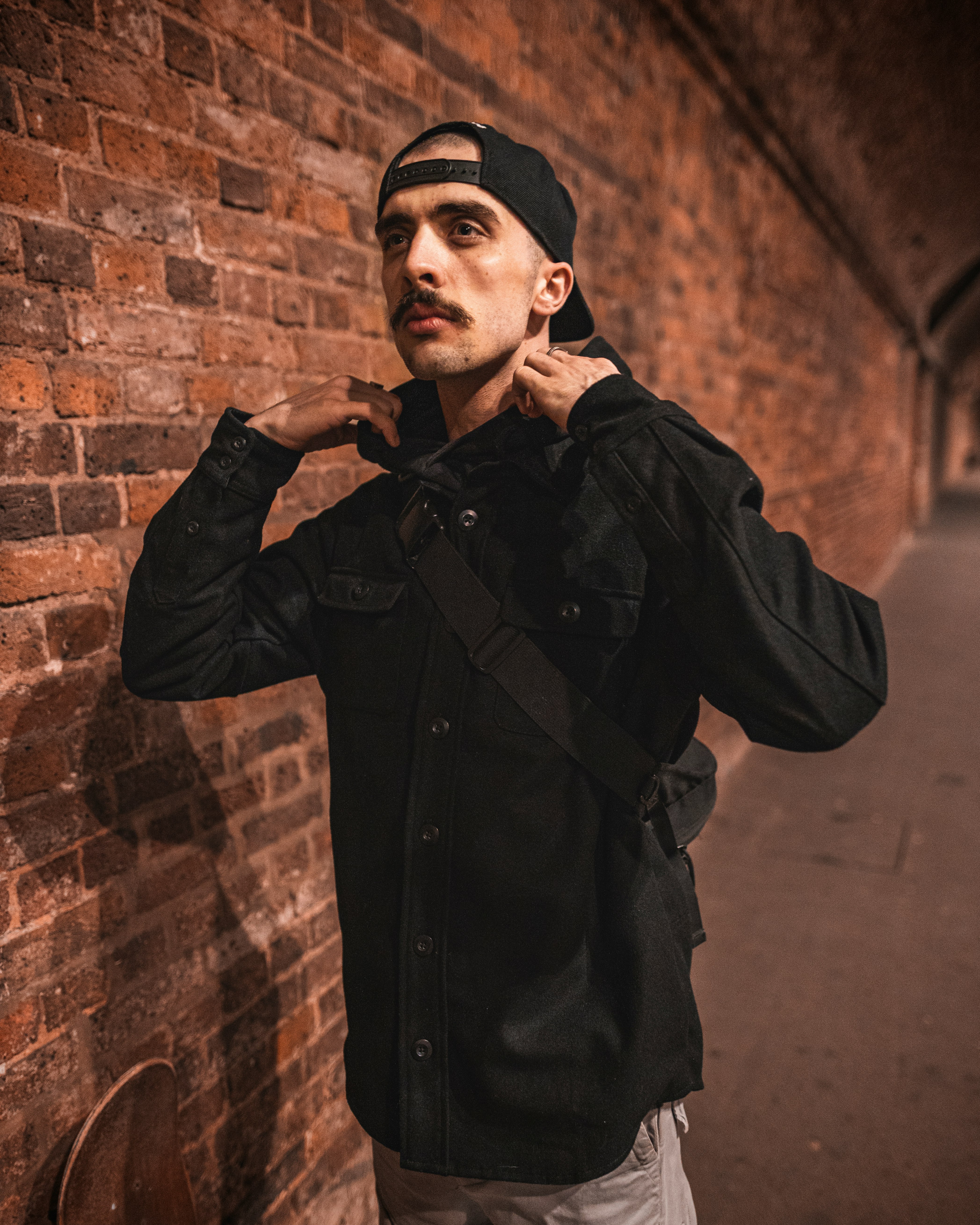 man in black coat and black cap standing beside brown brick wall