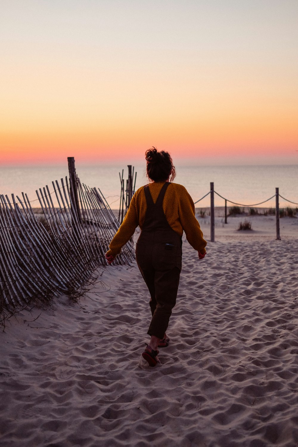 homem na jaqueta marrom andando na praia durante o pôr do sol