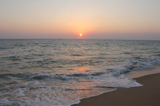 Sunset over a sandy Andalusian beach with gentle waves and a hint of orange sky.