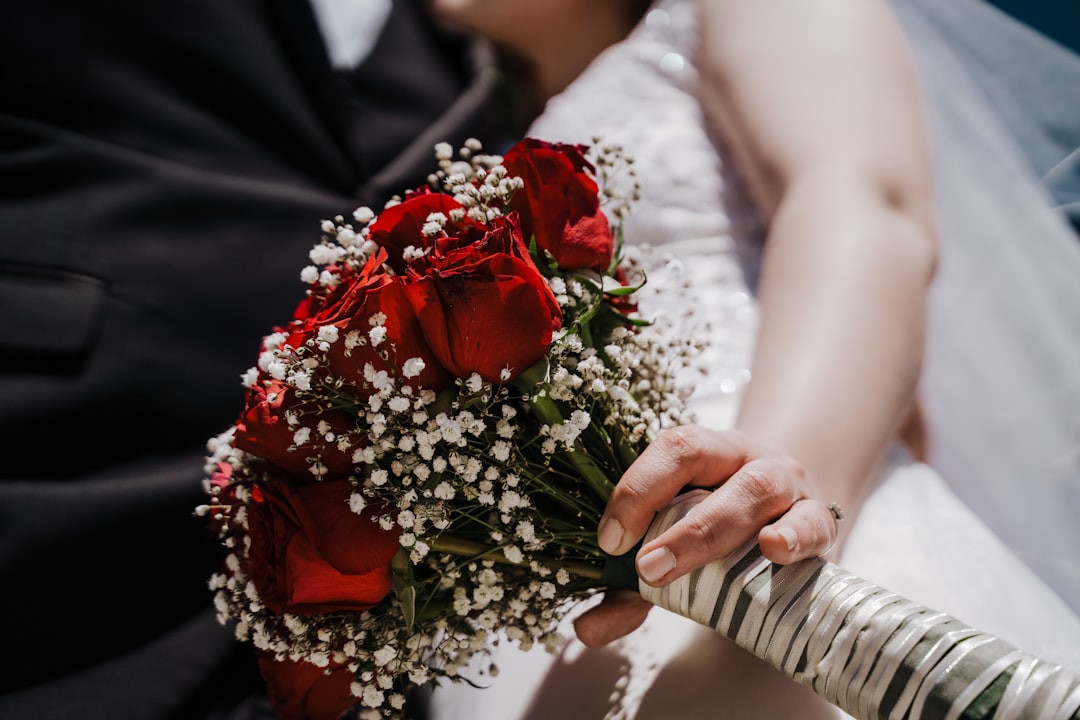 woman in white wedding dress holding red rose bouquet