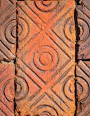 A close-up view of textured terracotta tiles with circular and diamond patterns, showing signs of aging and weathering.