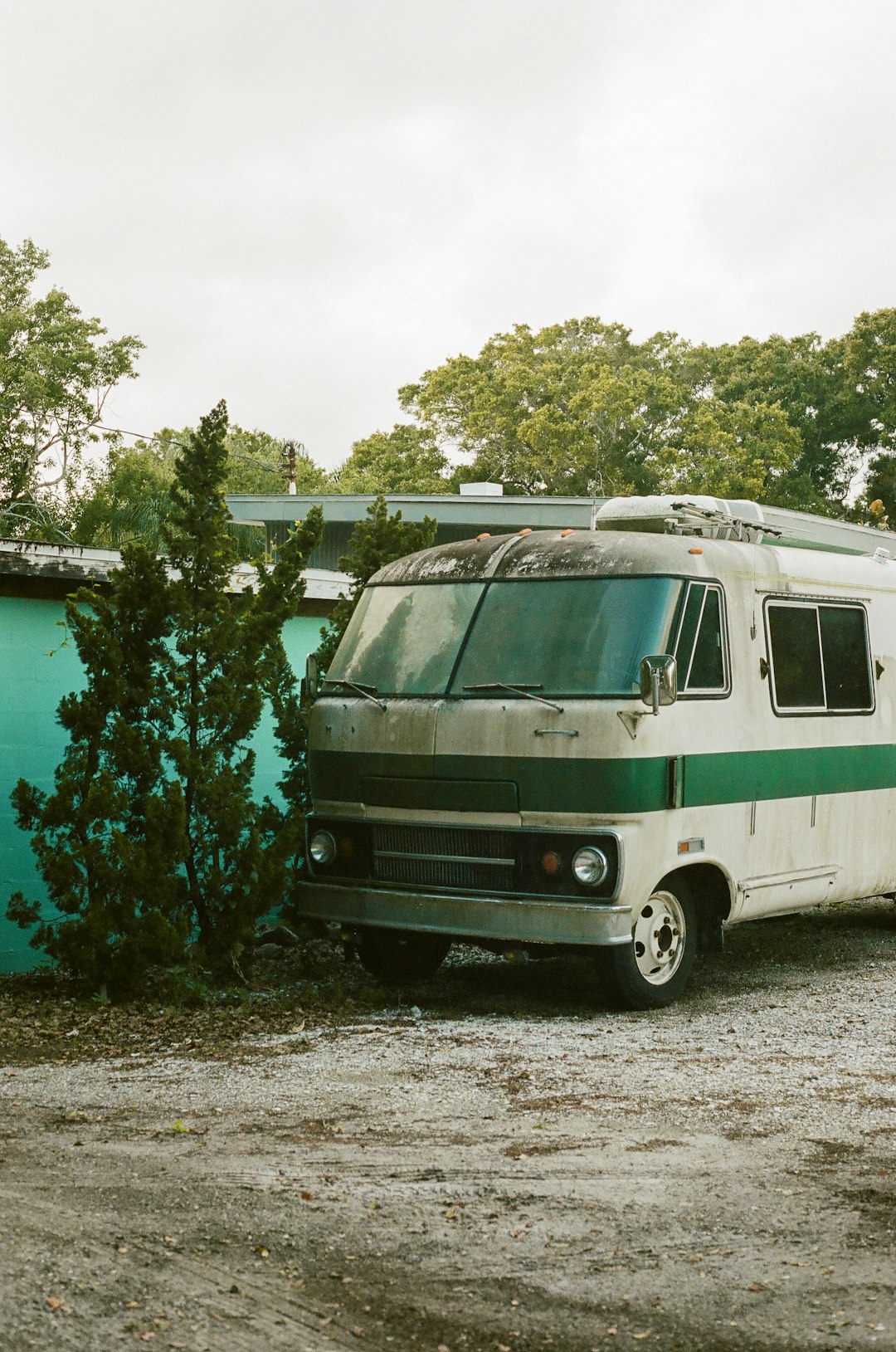 white and green rv trailer parked beside green trees during daytime