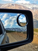 Electronic rearview mirror reflecting a bright sunny road with mountains in the distance.