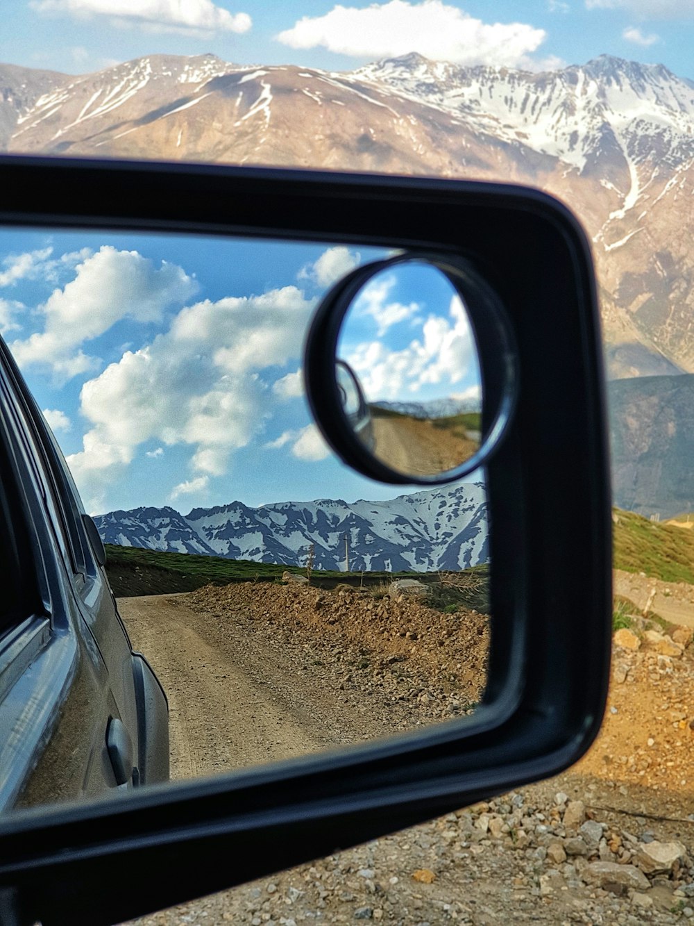 car side mirror showing car on road during daytime