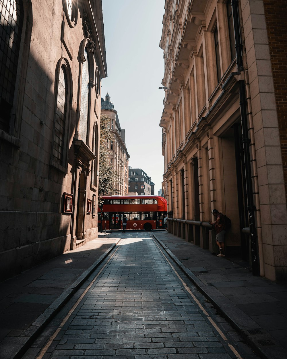 red bus in between of brown concrete buildings during daytime