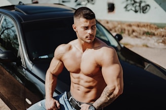 topless man in blue denim jeans sitting on car hood