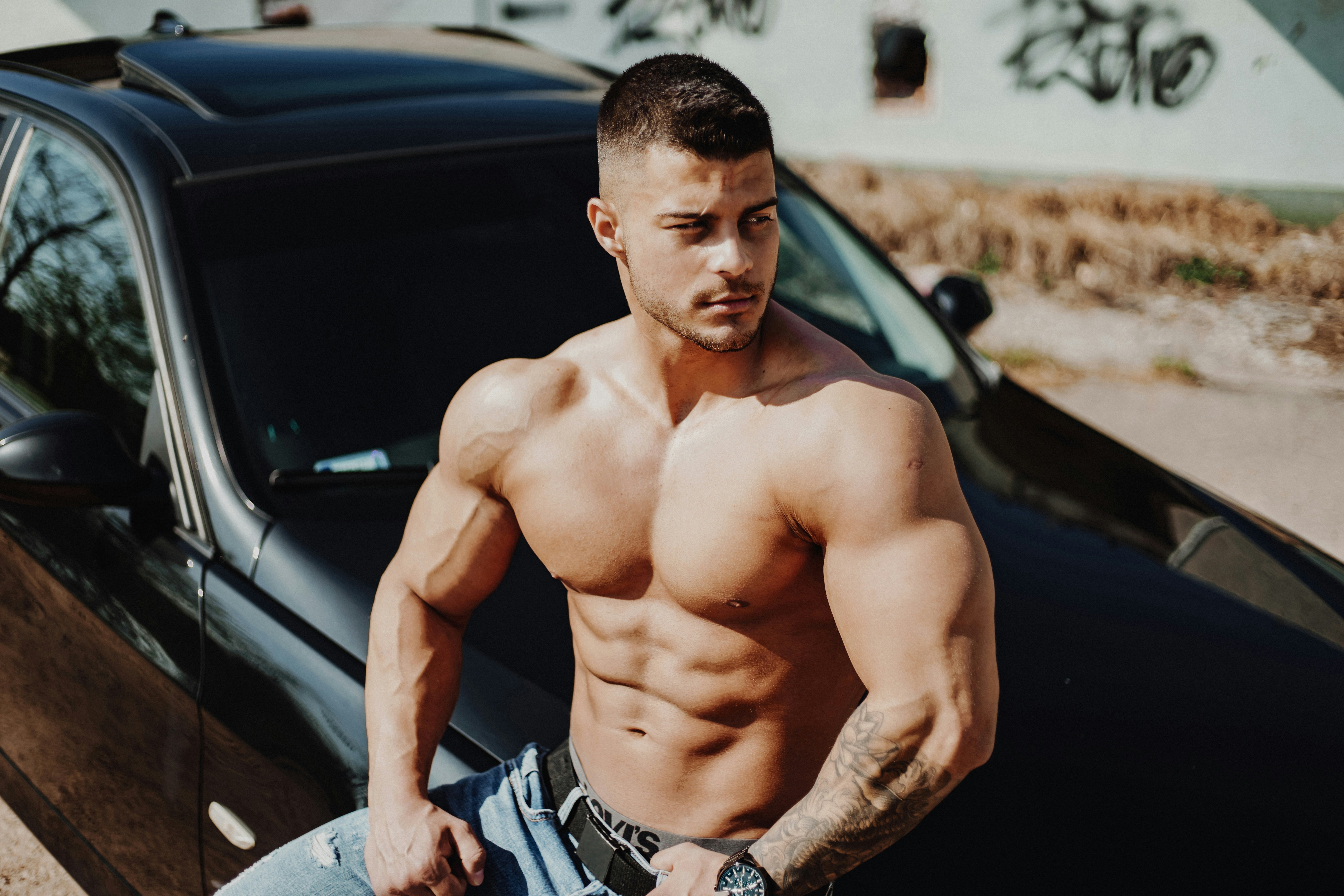 topless man in blue denim jeans sitting on car hood