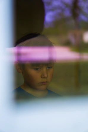 A boy looking out a window with a thoughtful expression, city ruins visible in the background.