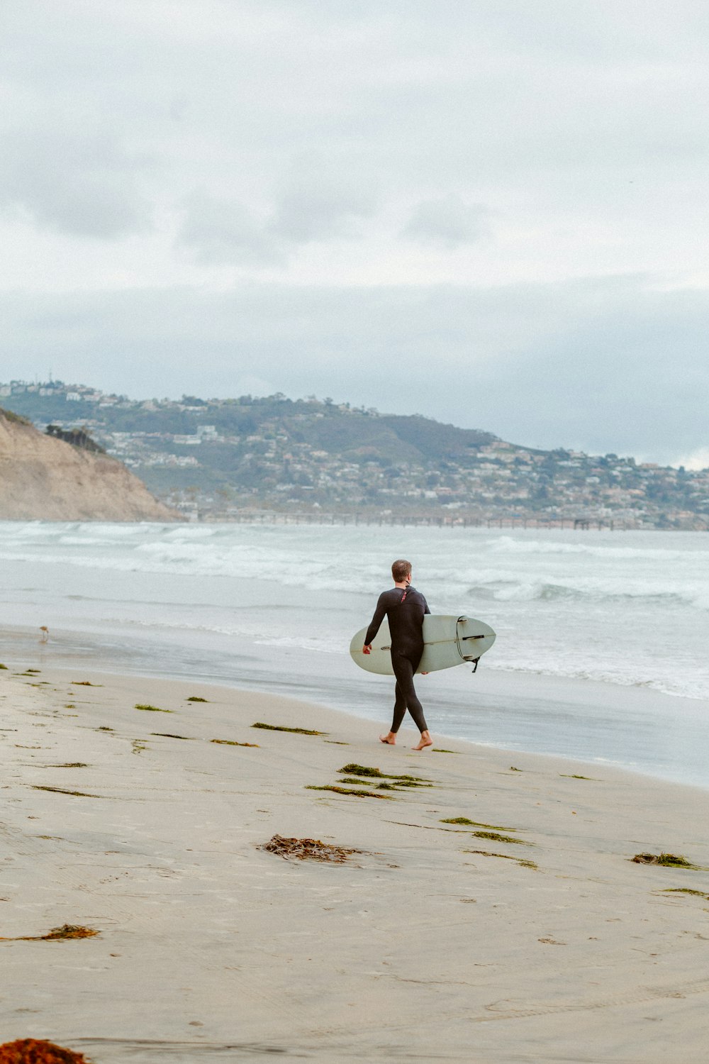 man in black shorts carrying white surfboard walking on beach during daytime