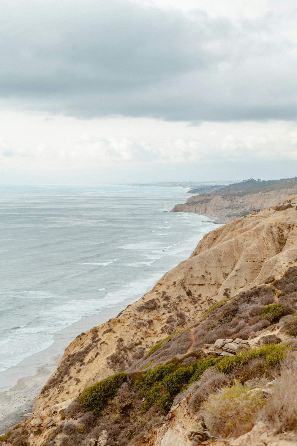 brown rocky mountain beside sea under white clouds during daytime