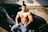 topless man in blue denim jeans sitting on car hood