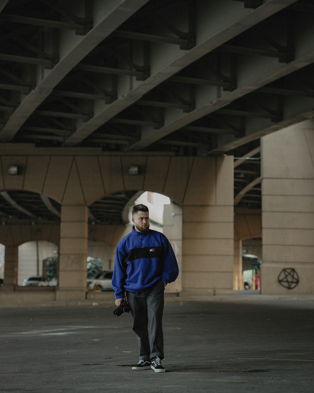 a man standing in a parking lot under a bridge