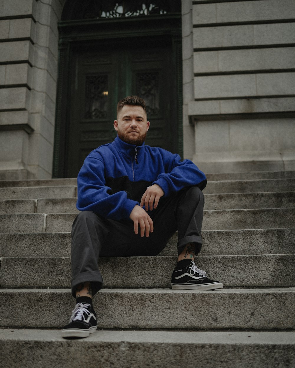 man in blue jacket sitting on gray concrete stairs