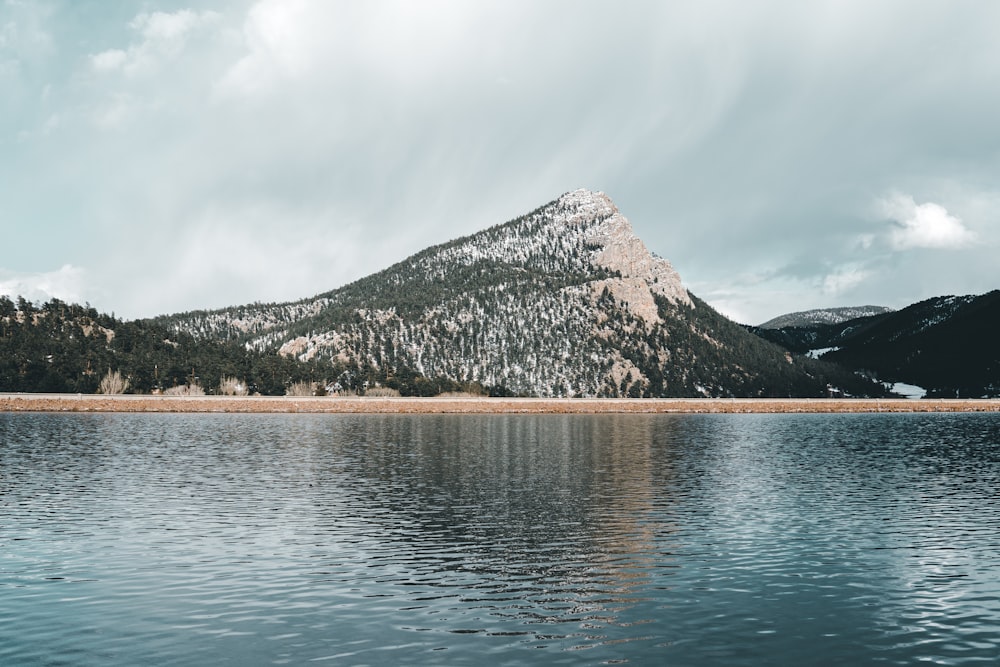 green and brown mountain beside body of water under white clouds during daytime