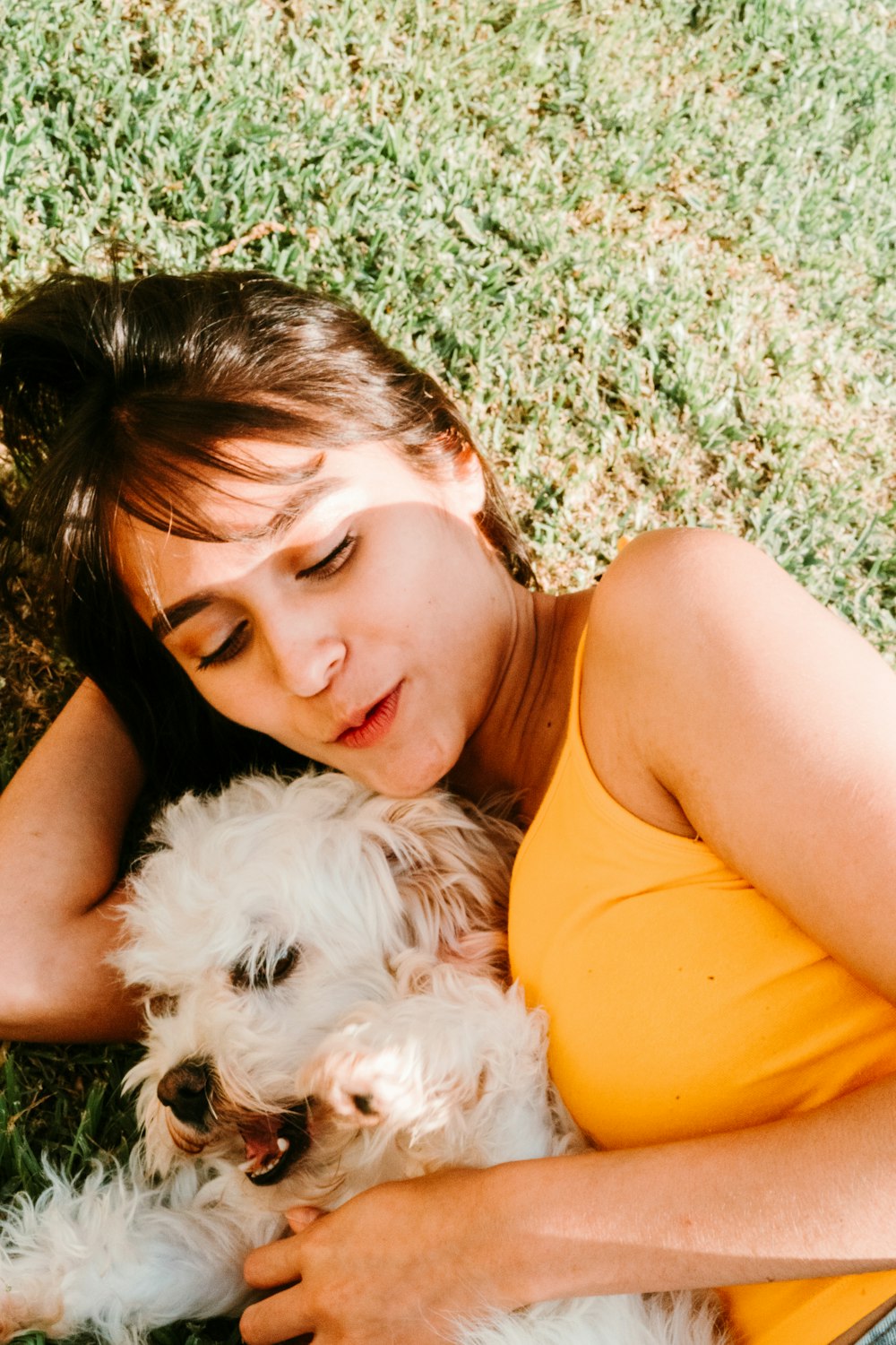 mulher na parte superior do tanque laranja deitada no campo verde da grama com o cão pequeno branco longo revestido