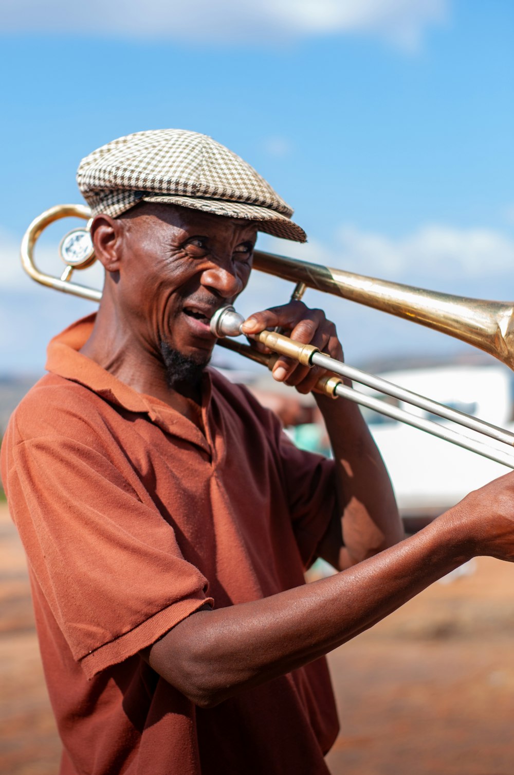 man in red polo shirt wearing brown hat holding brass trumpet during daytime