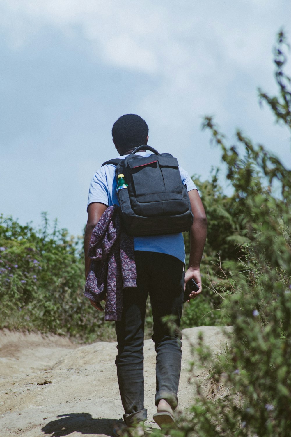 man in black and blue backpack walking on dirt road during daytime