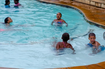 Children playing in a crystal-clear pool under a blue sky.