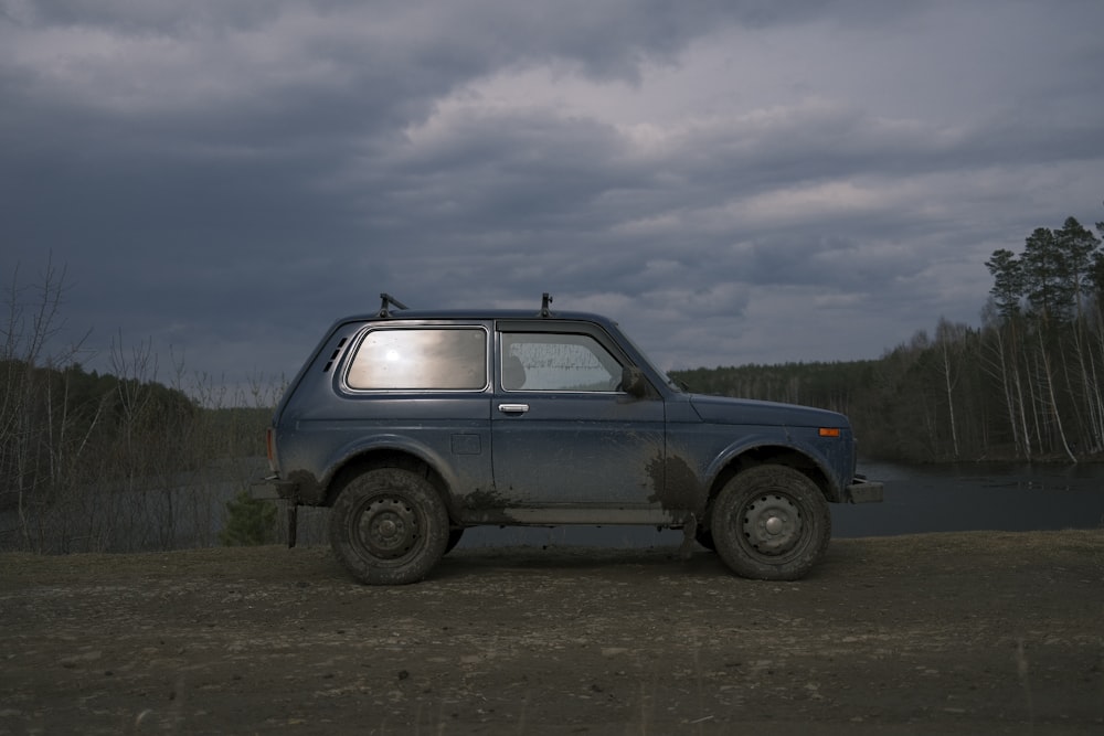 blue suv on brown dirt road under white clouds during daytime