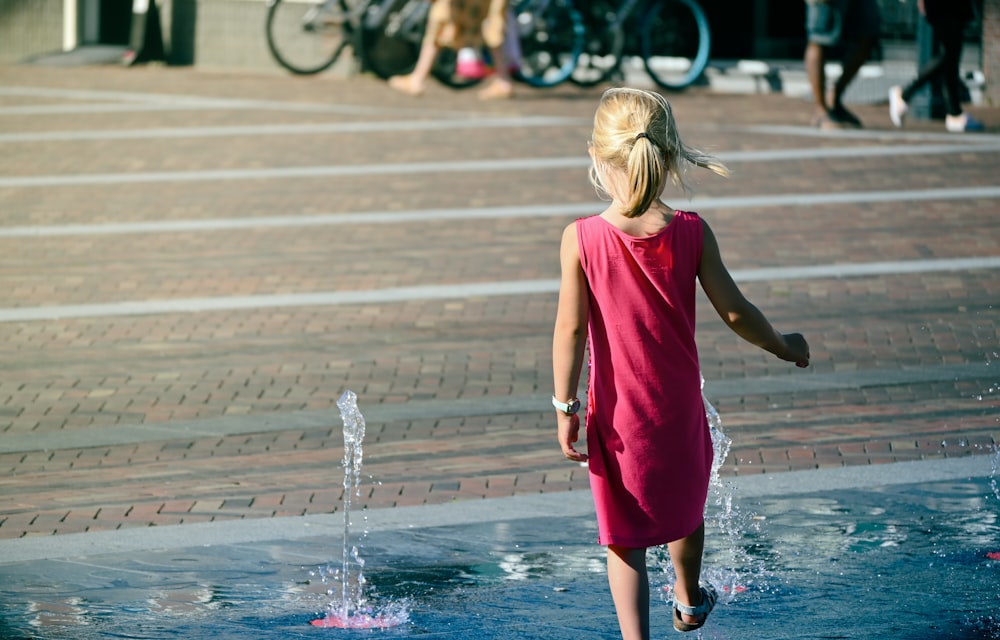 girl in red sleeveless dress standing on water fountain during daytime