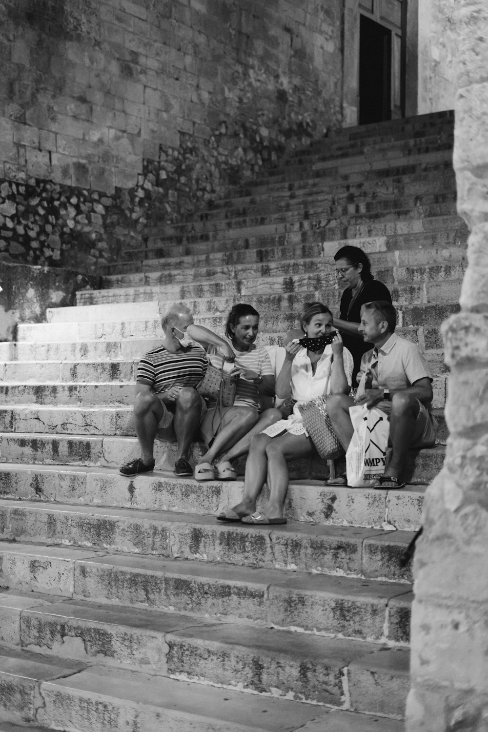 grayscale photo of 3 men sitting on concrete stairs