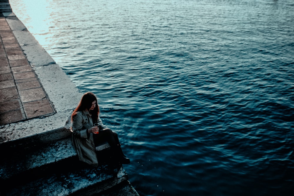 woman in black jacket sitting on concrete dock during daytime
