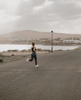 woman in black tank top and white pants running on gray asphalt road during daytime