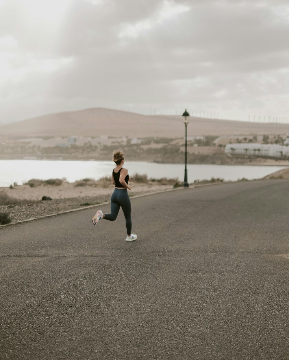 woman in black tank top and white pants running on gray asphalt road during daytime