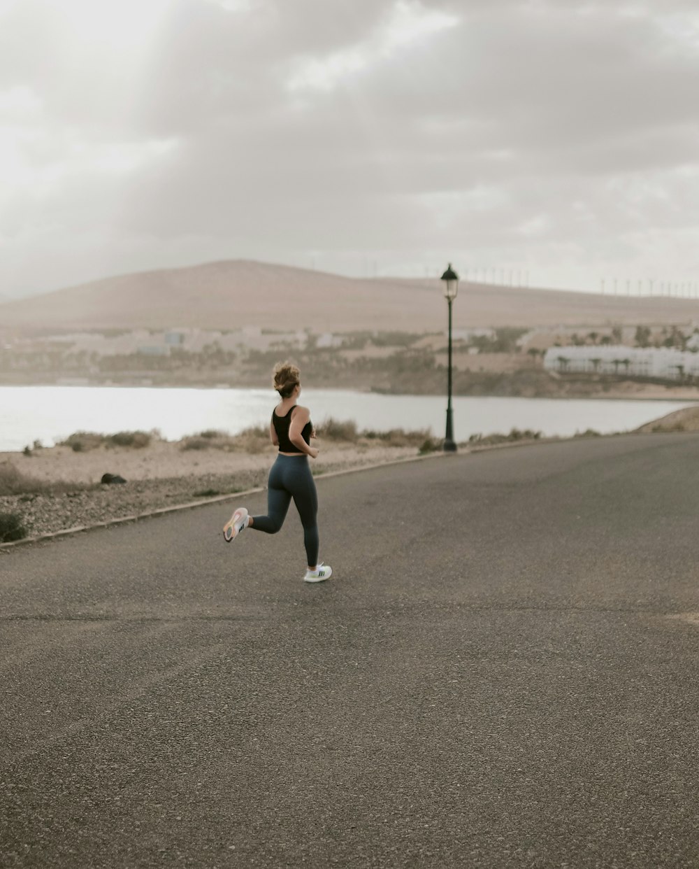 donna in canotta nera e pantaloni bianchi che corre sulla strada asfaltata grigia durante il giorno