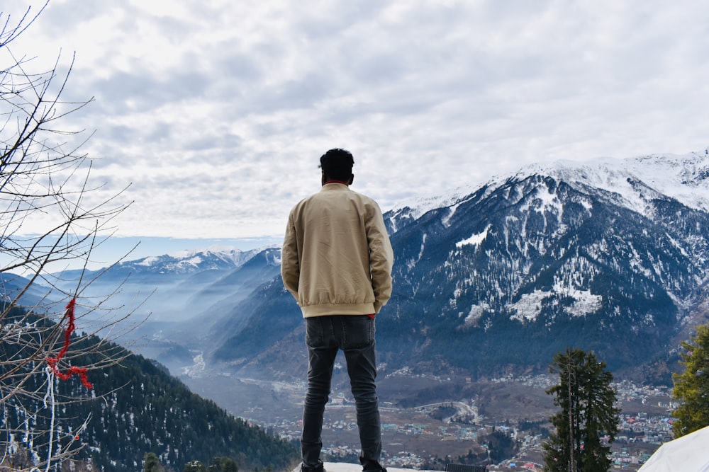 man in beige jacket and black pants standing on top of mountain during daytime